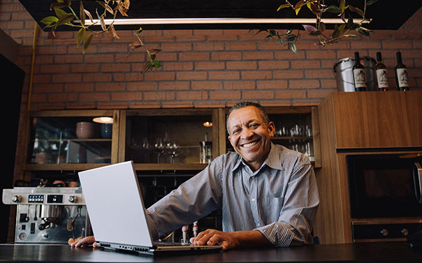 mature cafe owner smiling in front of laptop
